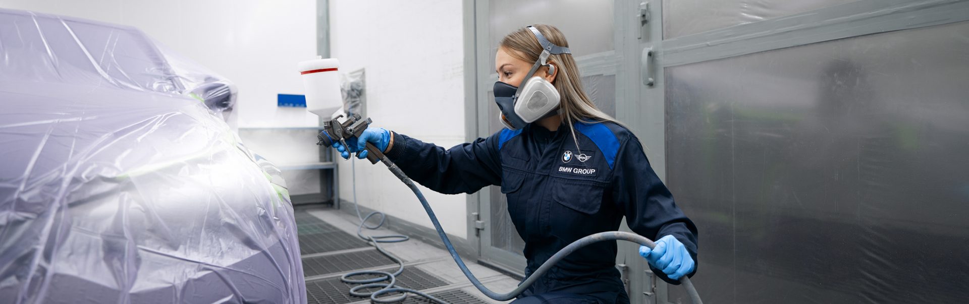 A female apprentice as car sprayer at the BMW Group applying paint to a car using a spray gun in a workshop.