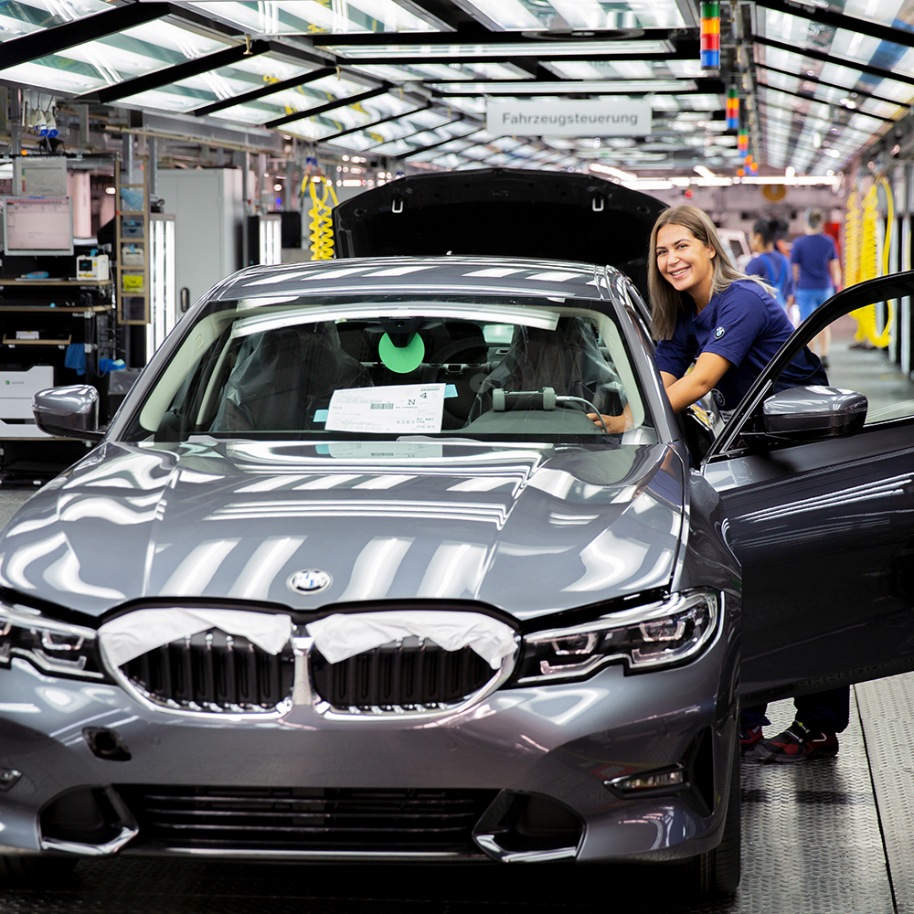 BMW car being assembled in a factory with a smiling apprentice as production mechanic at the BMW Group.