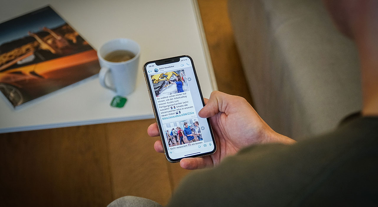 A hand holding a smartphone with the screen showing an open BMW newsletter.