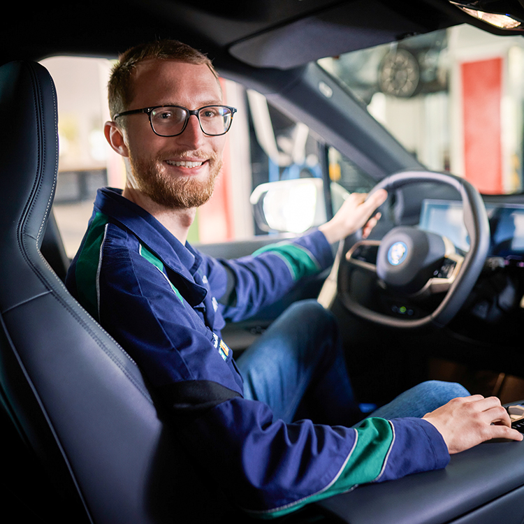 An electrical engineering instructor at the BMW Group sits smiling in the driver's seat of a BMW.