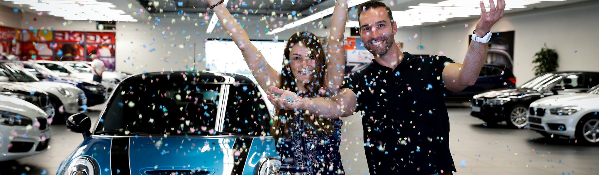 Happy couple celebrating with confetti at a BMW car dealership.