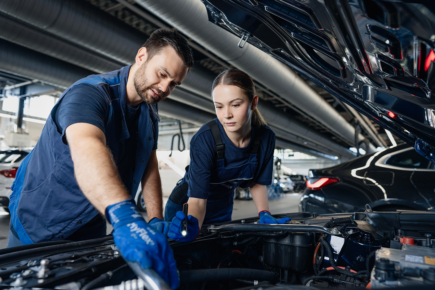Two trainees are working on a motor in a BMW workshop.