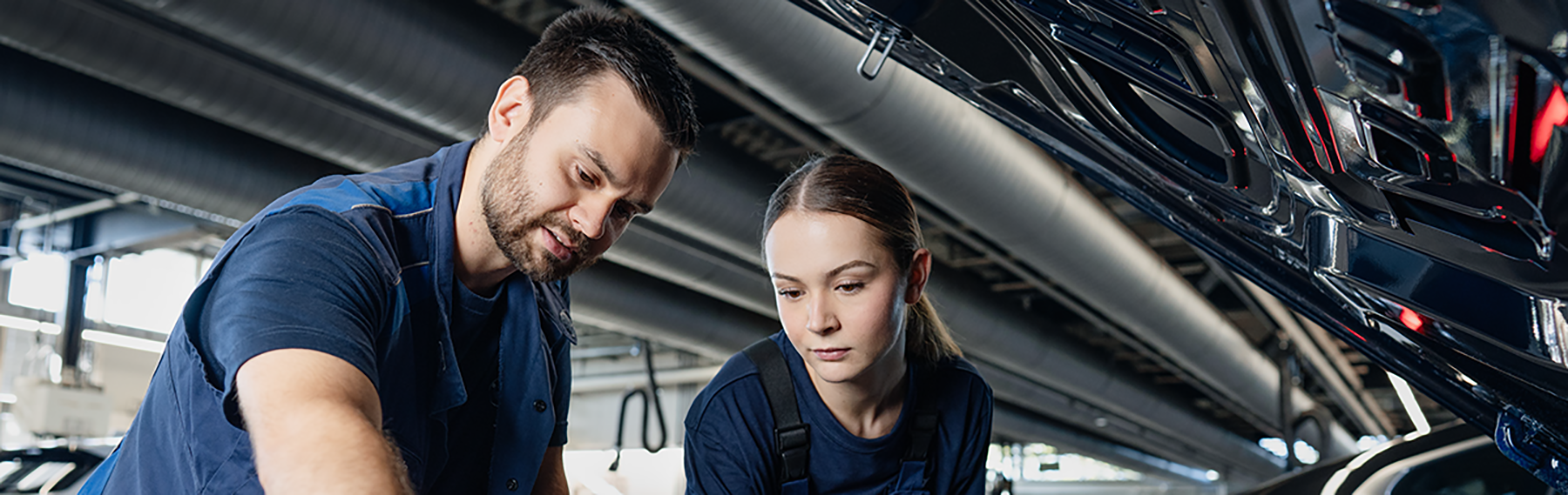 Two trainees are working on a motor in a BMW workshop.