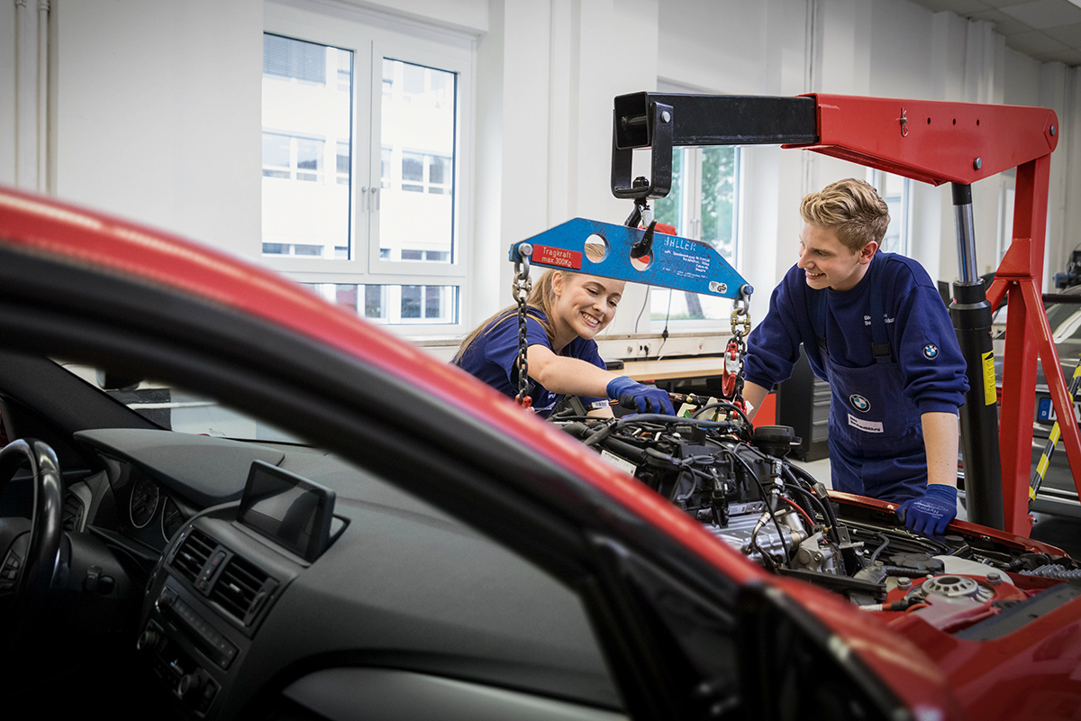 Two mechatronics engineers work in the engine compartment of a car in a BMW Group workshop.