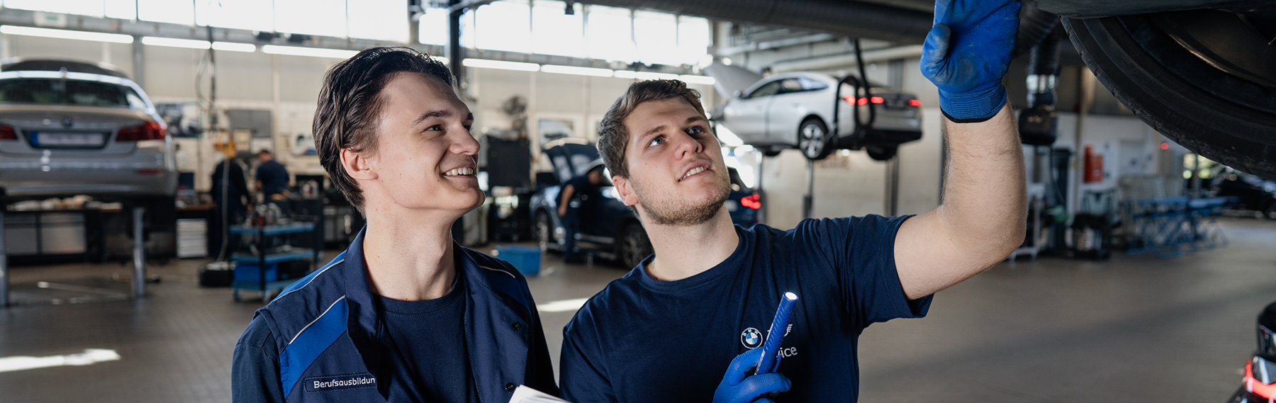 Two apprentices in the BMW workshop laugh and work together.