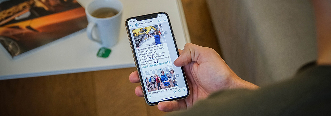 A hand holding a smartphone with the screen showing an open BMW Pupil newsletter.
