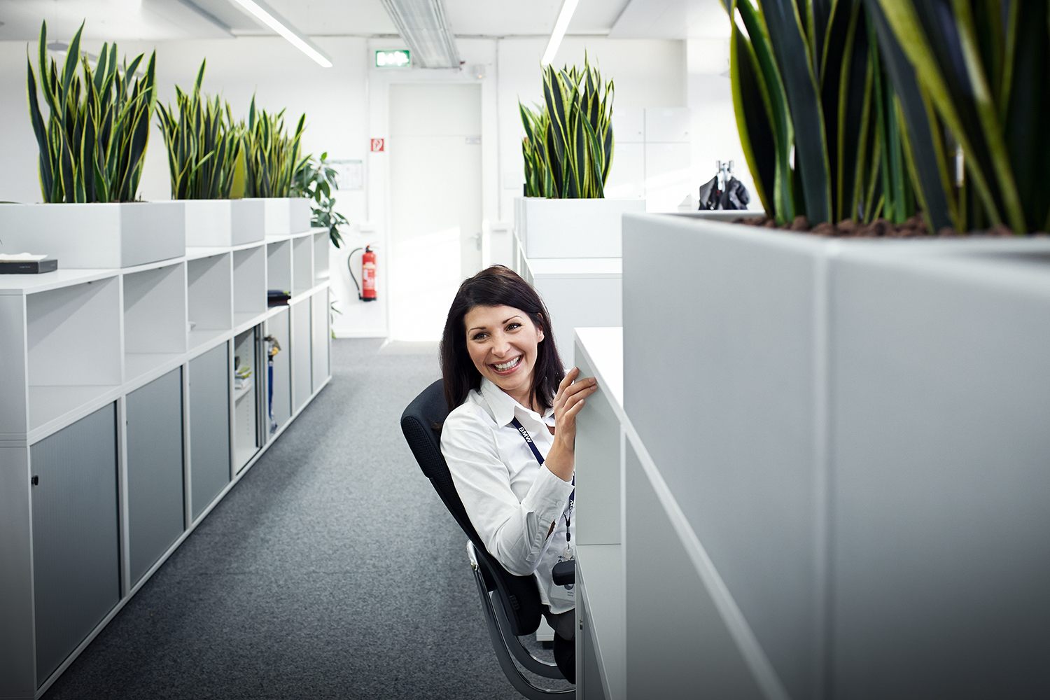 Smiling trainee marketing communications specialist at the BMW Group in a modern office with plants.