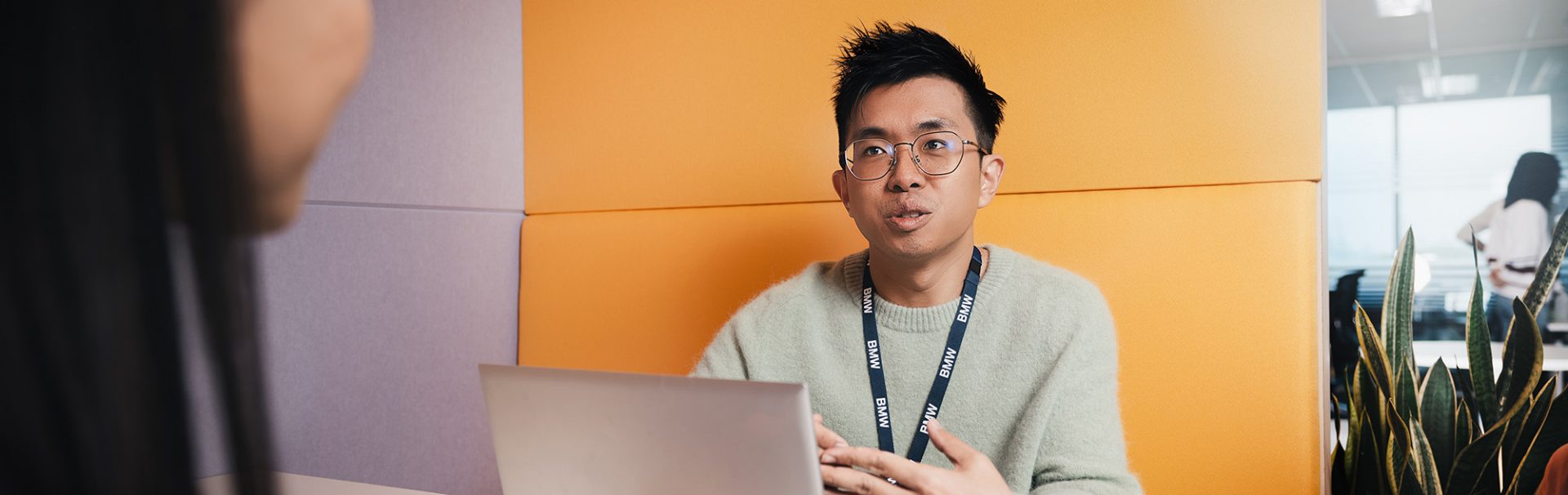 Smiling trainee marketing communications specialist at the BMW Group in a modern office with plants.
