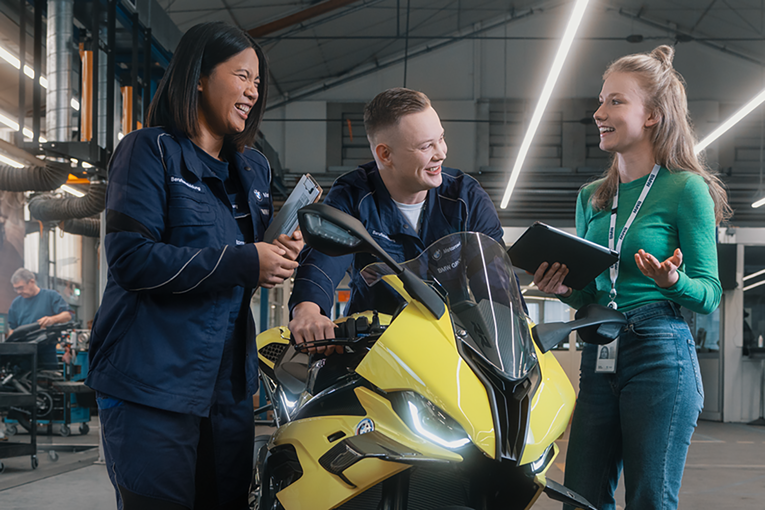 Three trainees stand next to a motorcycle and laugh.