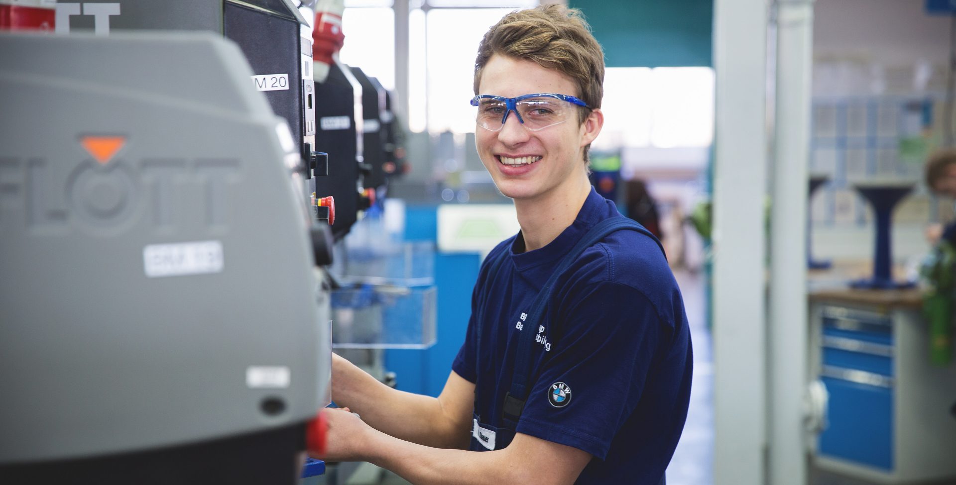 Smiling mechatronics trainee at the BMW Group while working on a machine.