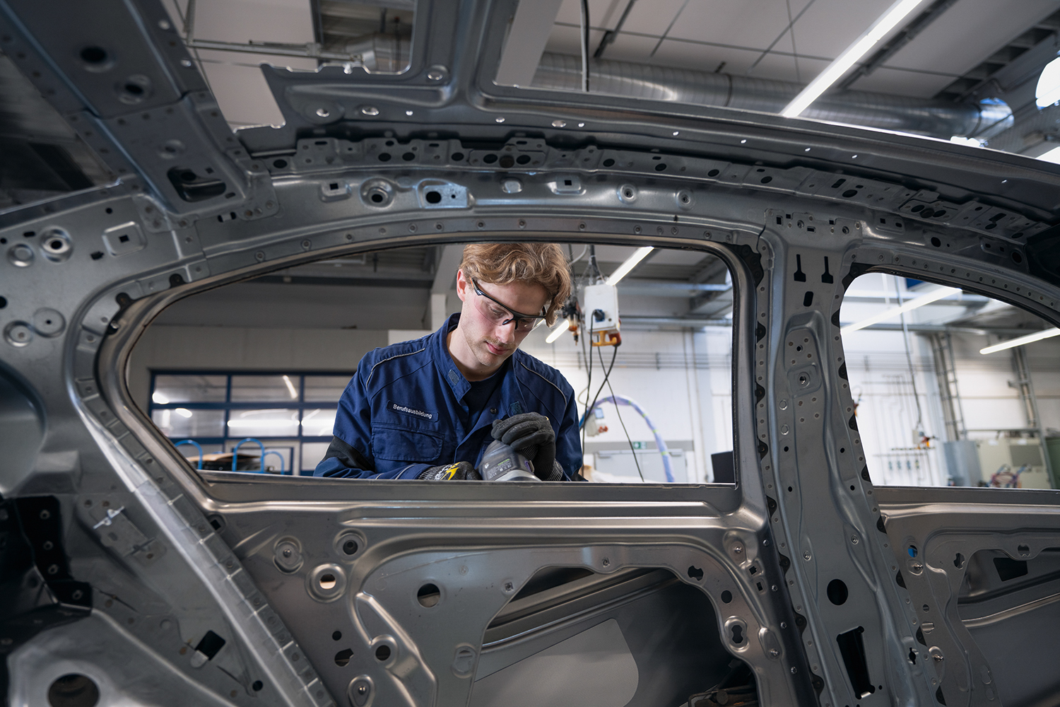A trainee body and vehicle construction mechanic at the BMW Group carries out precise work on a vehicle frame.