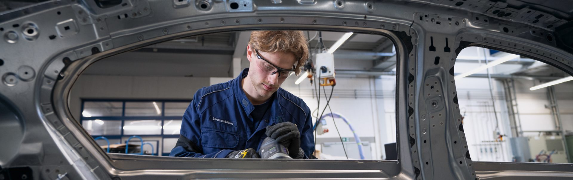 A trainee body and vehicle construction mechanic at the BMW Group carries out precise work on a vehicle frame.