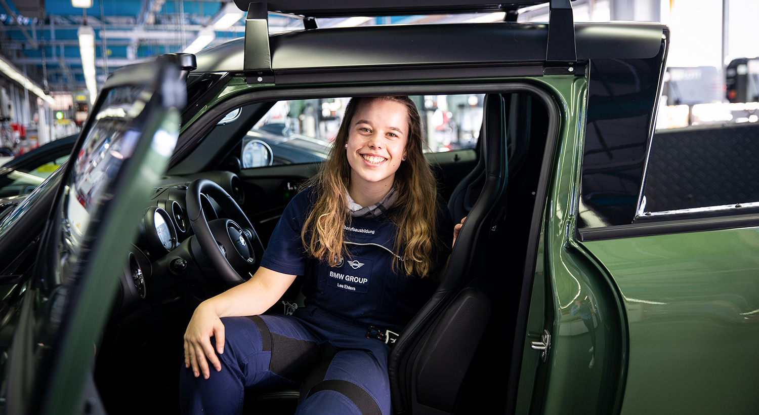 Apprentice body and vehicle mechanic in the BMW workshop, sitting proudly in a car.