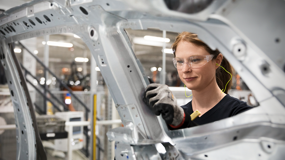 Apprentice in vehicle construction technology with protective equipment at the BMW Group works on a car body.