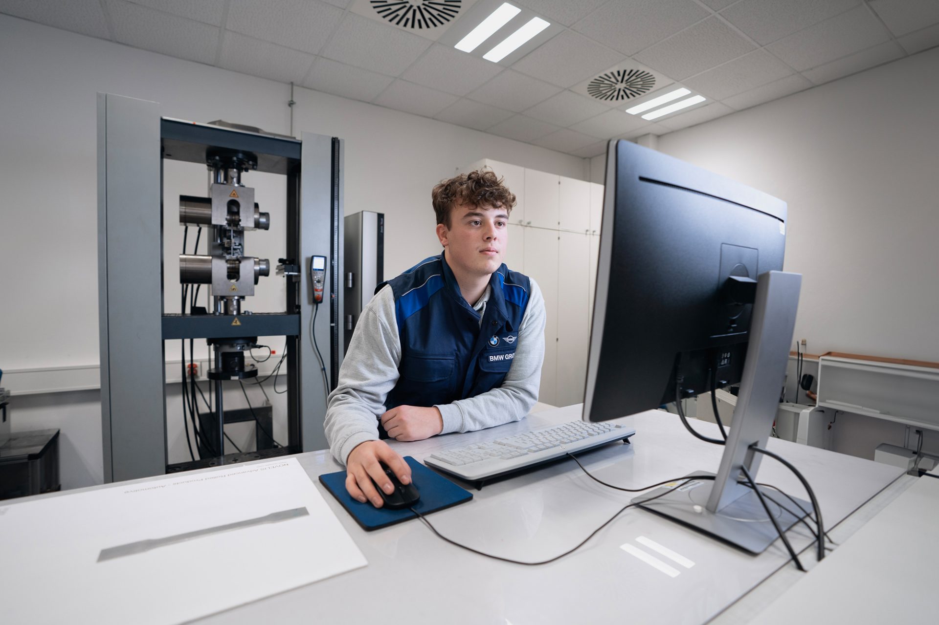 Trainee plastics and rubber technologist at the BMW Group wearing safety goggles operates a robot arm in a production environment.