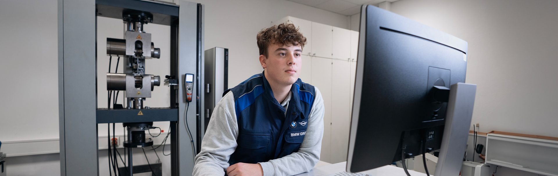 Trainee plastics and rubber technologist at the BMW Group wearing safety goggles operates a robot arm in a production environment.