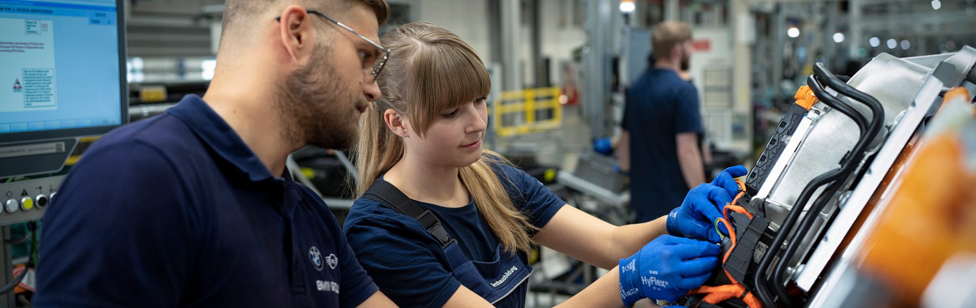 A apprentice as production mechanic smiling while inspecting a car in a BMW Group factory.