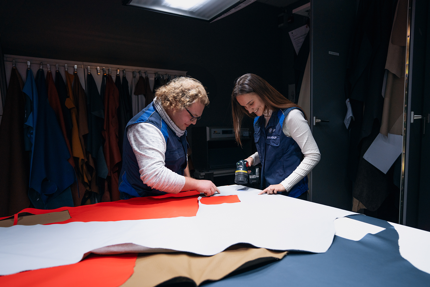 Two vehicle interior mechanics engaged in a collaborative design process, working with fabric and tools in a creative workspace at the BMW Group.