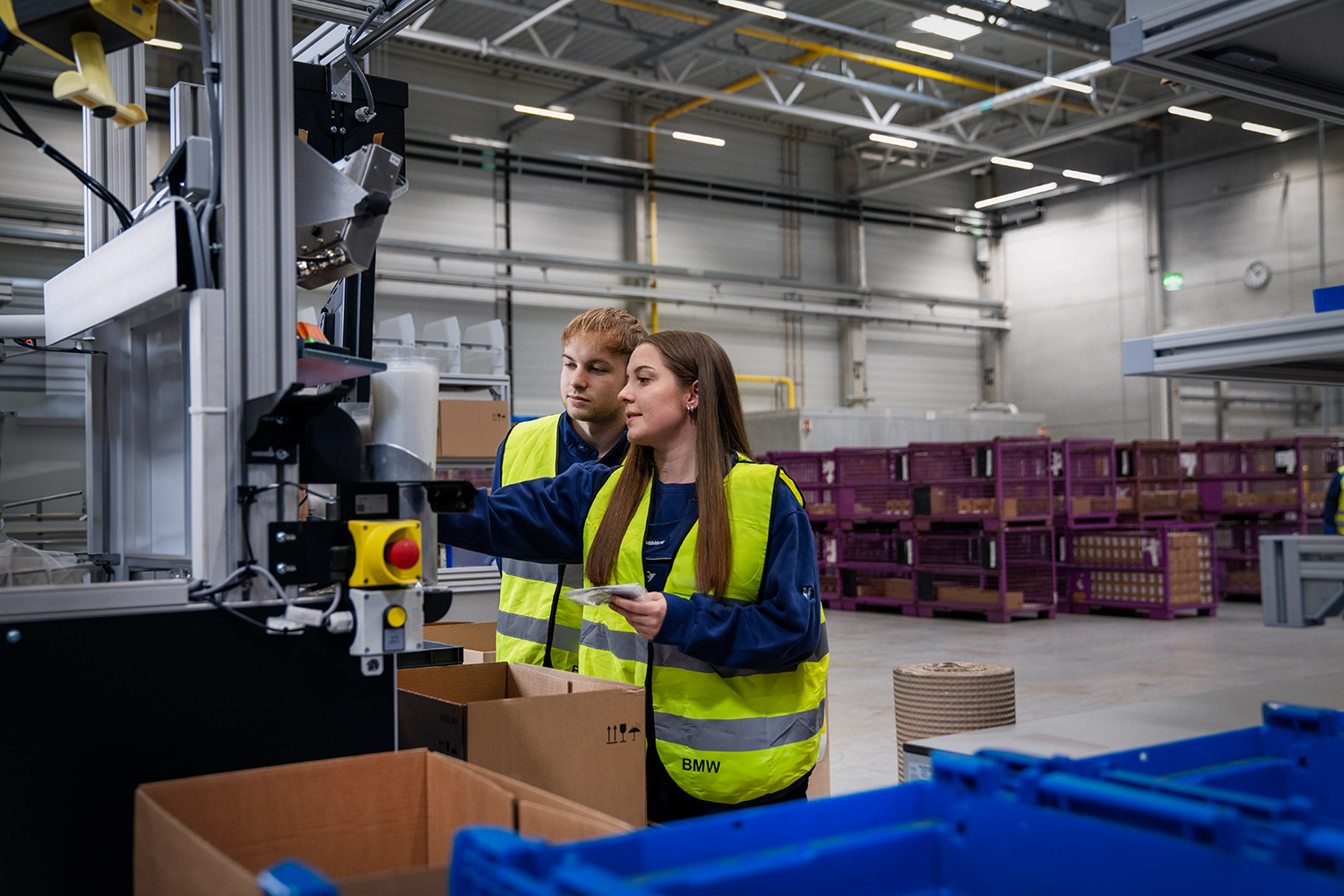 Two trainees are working on a machine in a BMW warehouse.