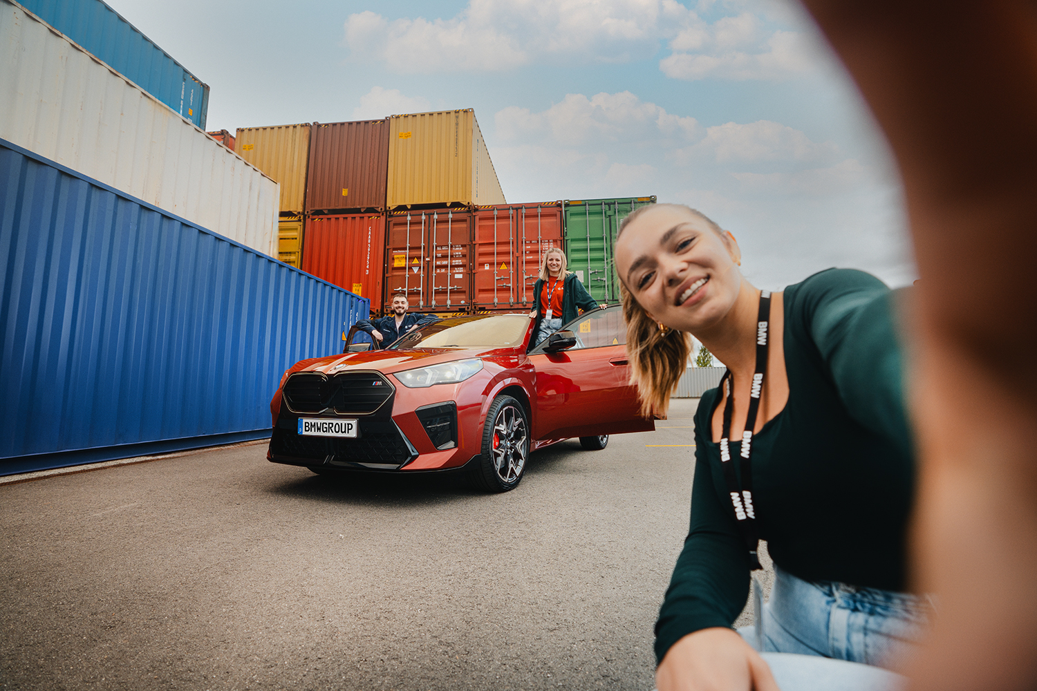 BMW dual students posing with a red BMW X2 and colourful shipping containers.