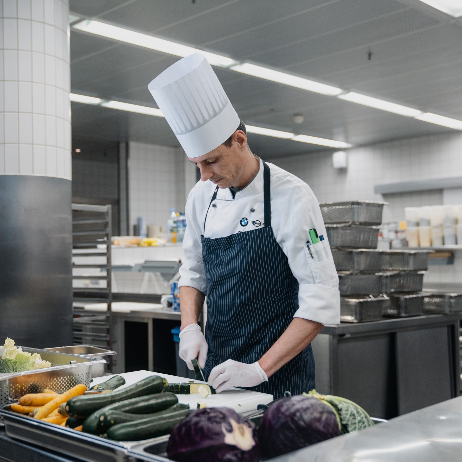 A professional cooking environment with a chef preparing food and fresh vegetables in the BMW Group Company kitchen.