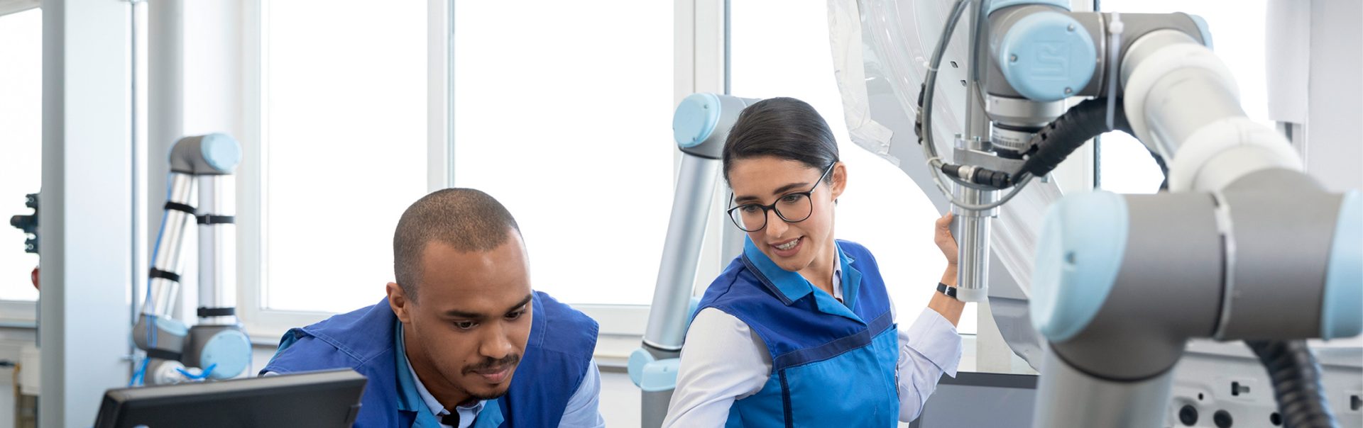 Two automation technologists collaborating in a robotics lab, working with a robotic arm.