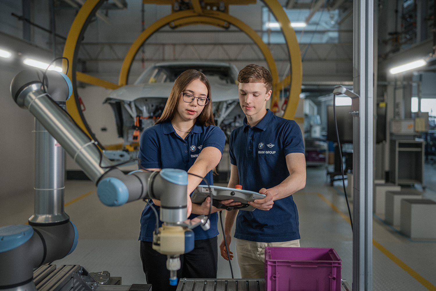 Two students are working on a machine in a production hall.