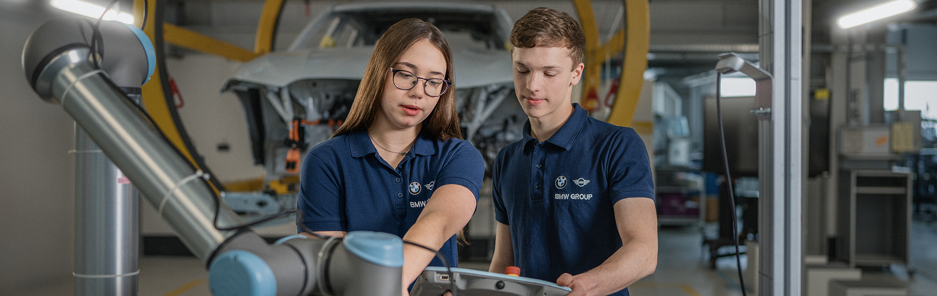Two students are working on a machine in a production hall.