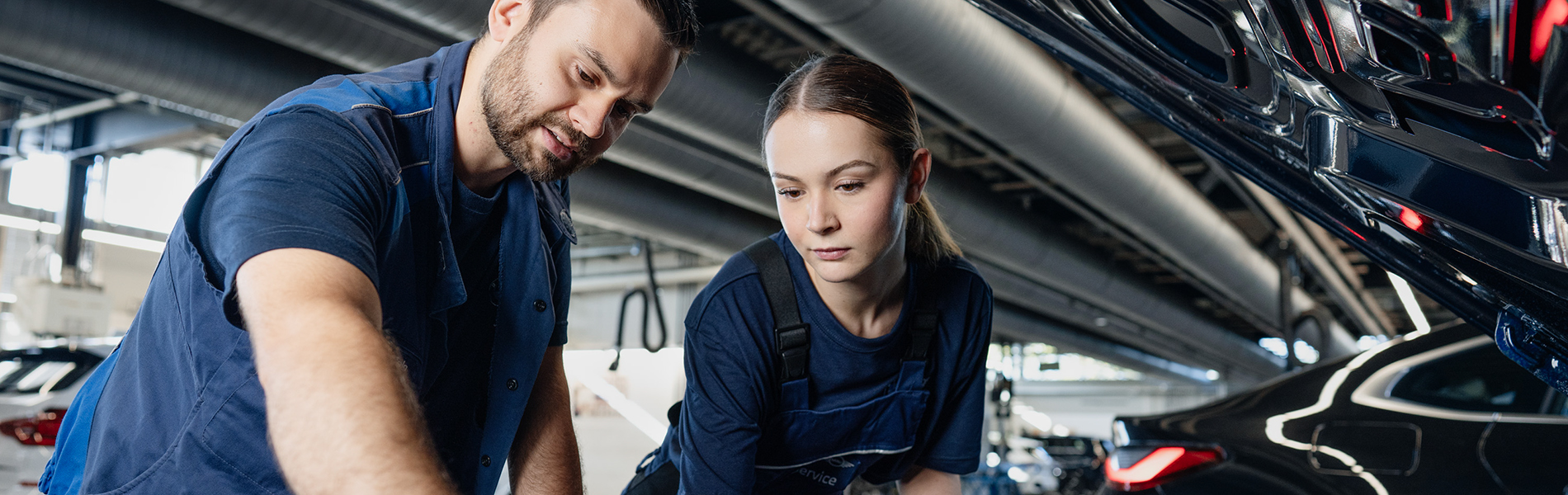 Apprentice and trainer working on the engine of a vehicle