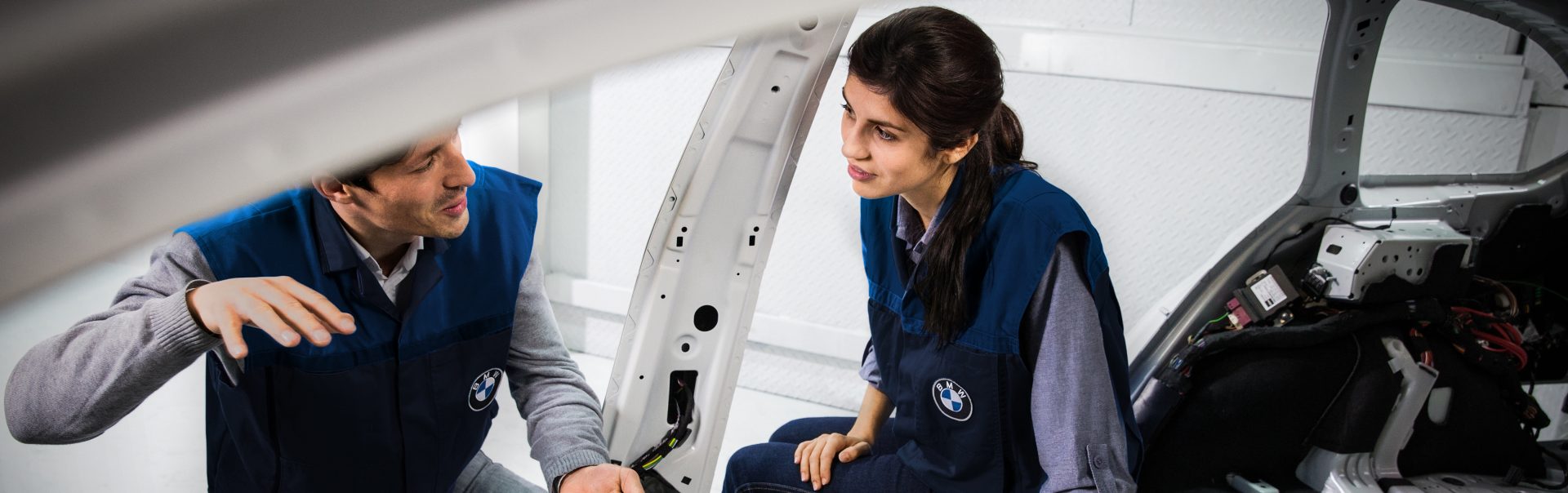 A dual student in design at the BMW Group sits in a vehicle body and chats with her trainer.