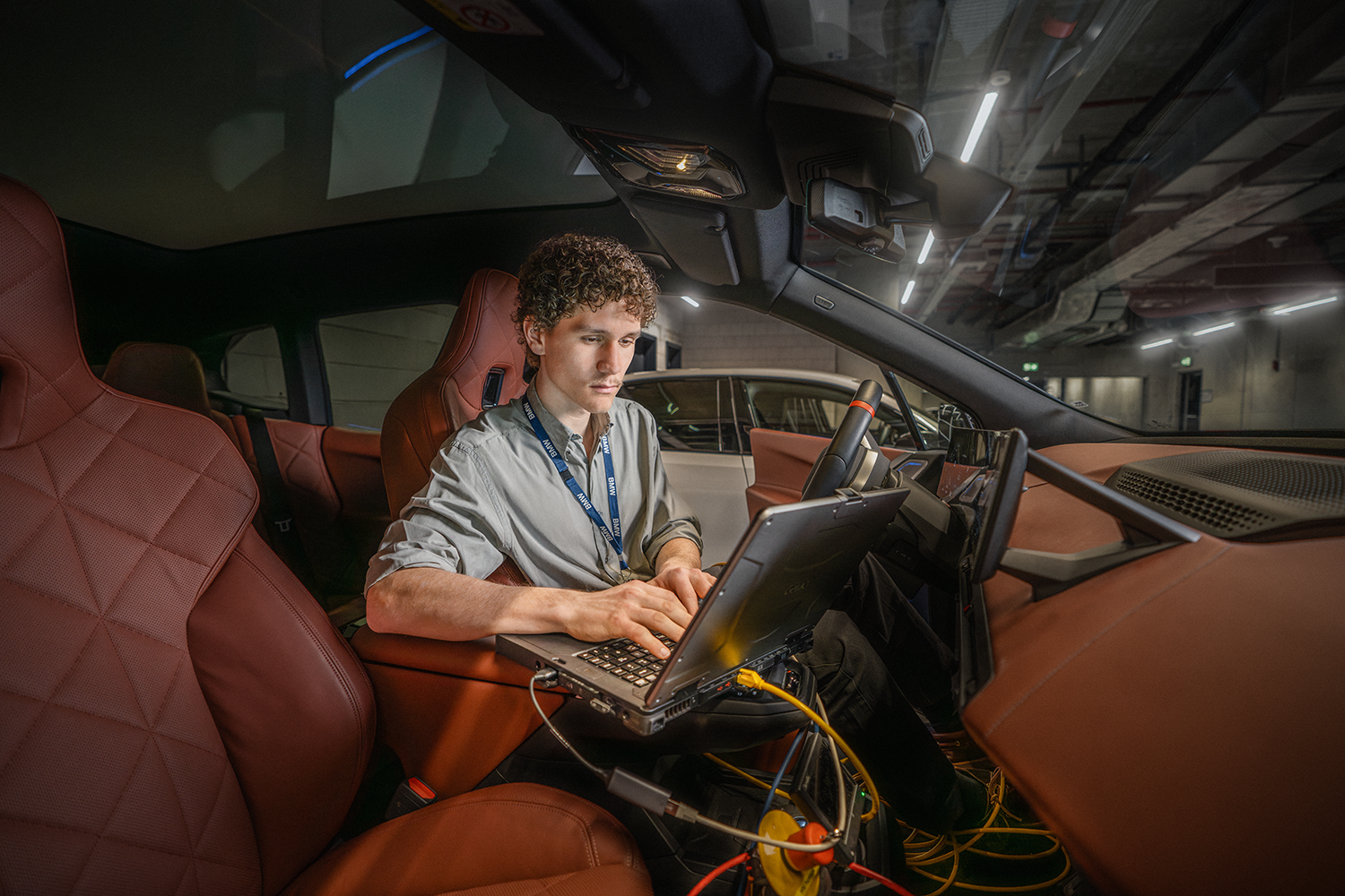 A male student sits in the driver’s seat of a BMW and works at the computer.