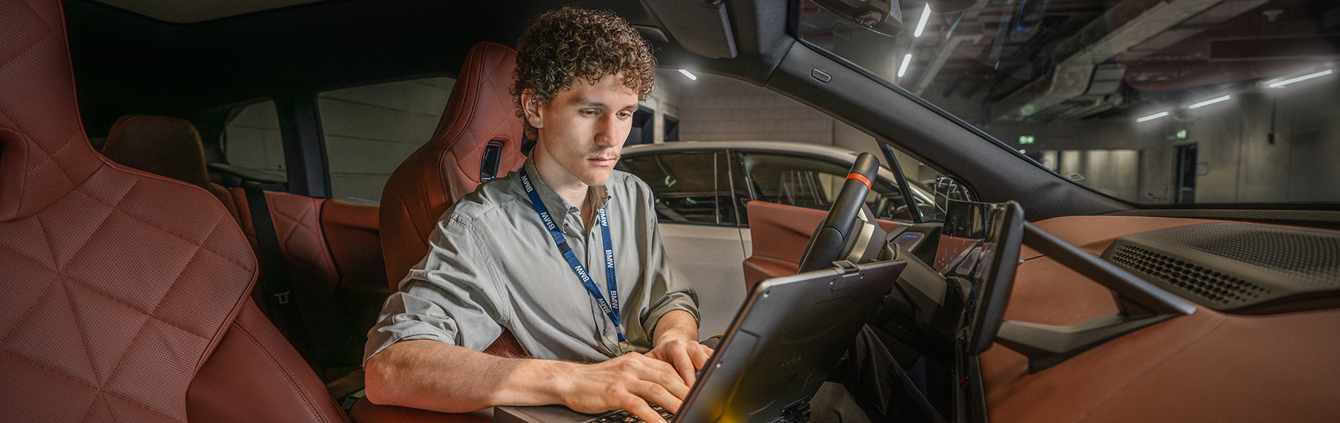 A student sits in the driver’s seat of a BMW and works at the computer.