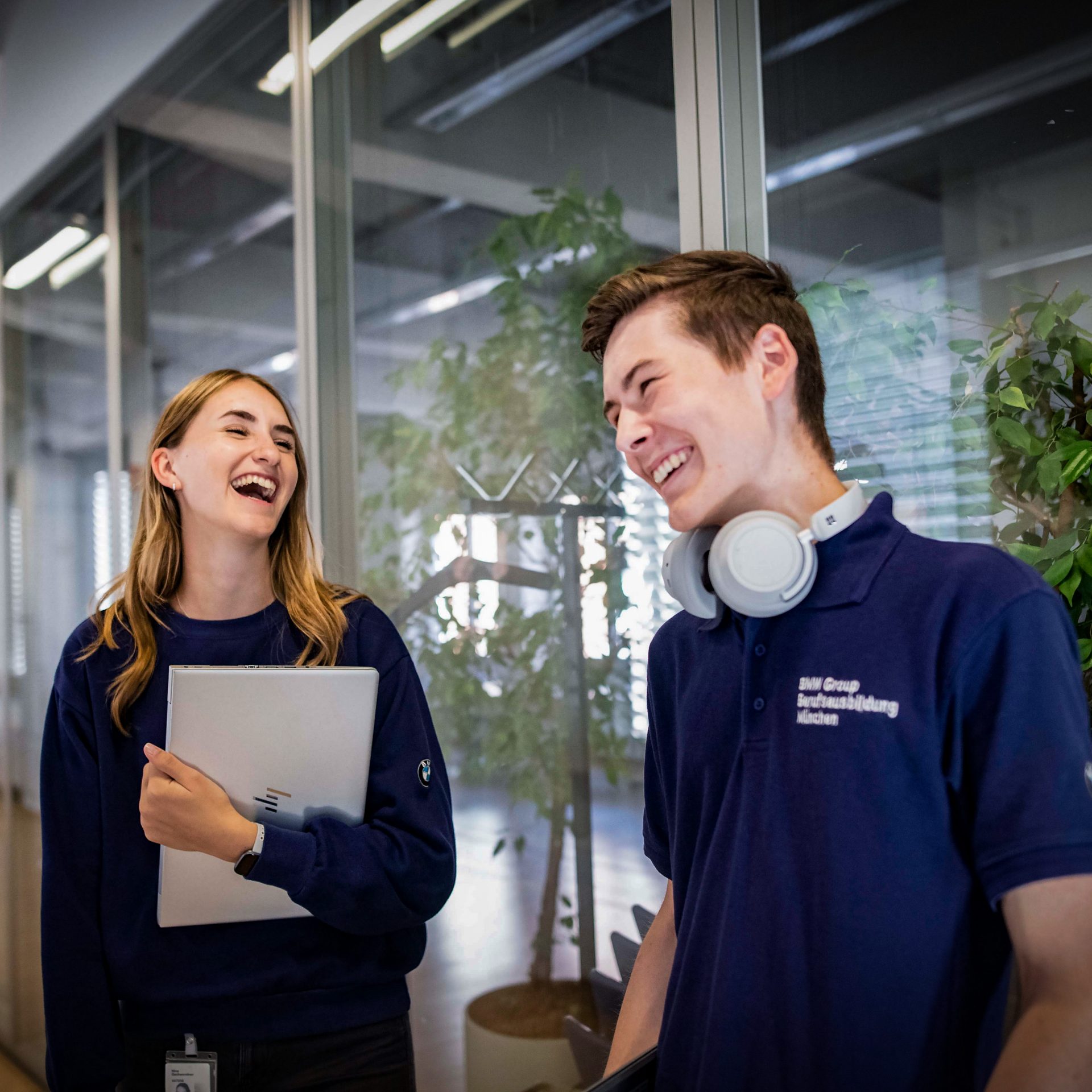 Two young apprentices laughing together in an office environment, showcasing a positive workplace atmosphere at the BMW Group.