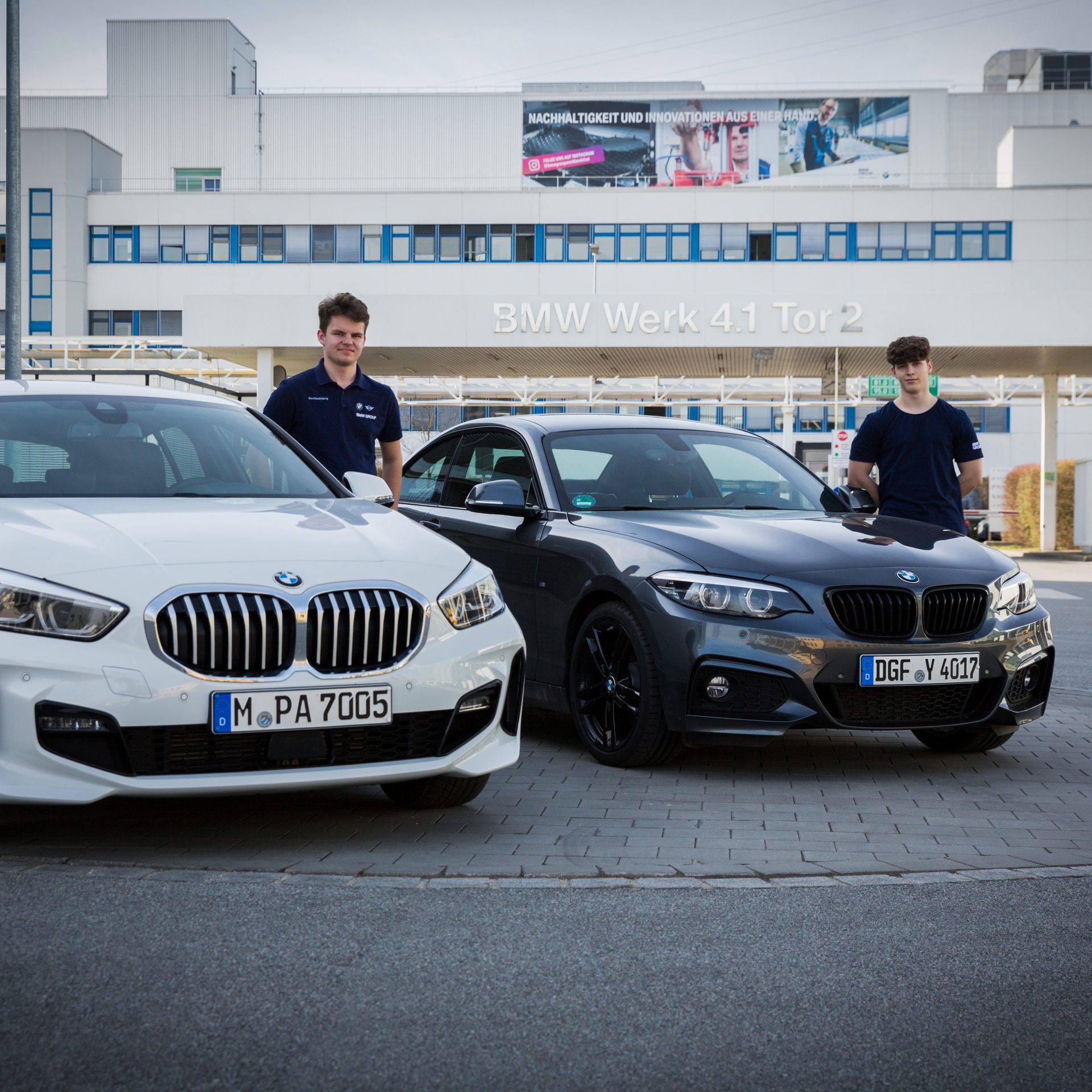 Two apprentices standing next to their BMW Cars.