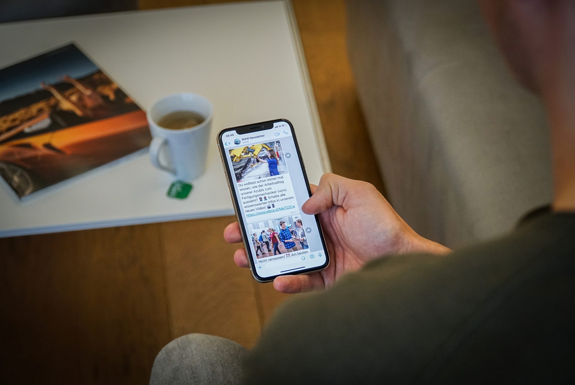 A hand holding a smartphone with the screen showing an open BMW Pupil newsletter.