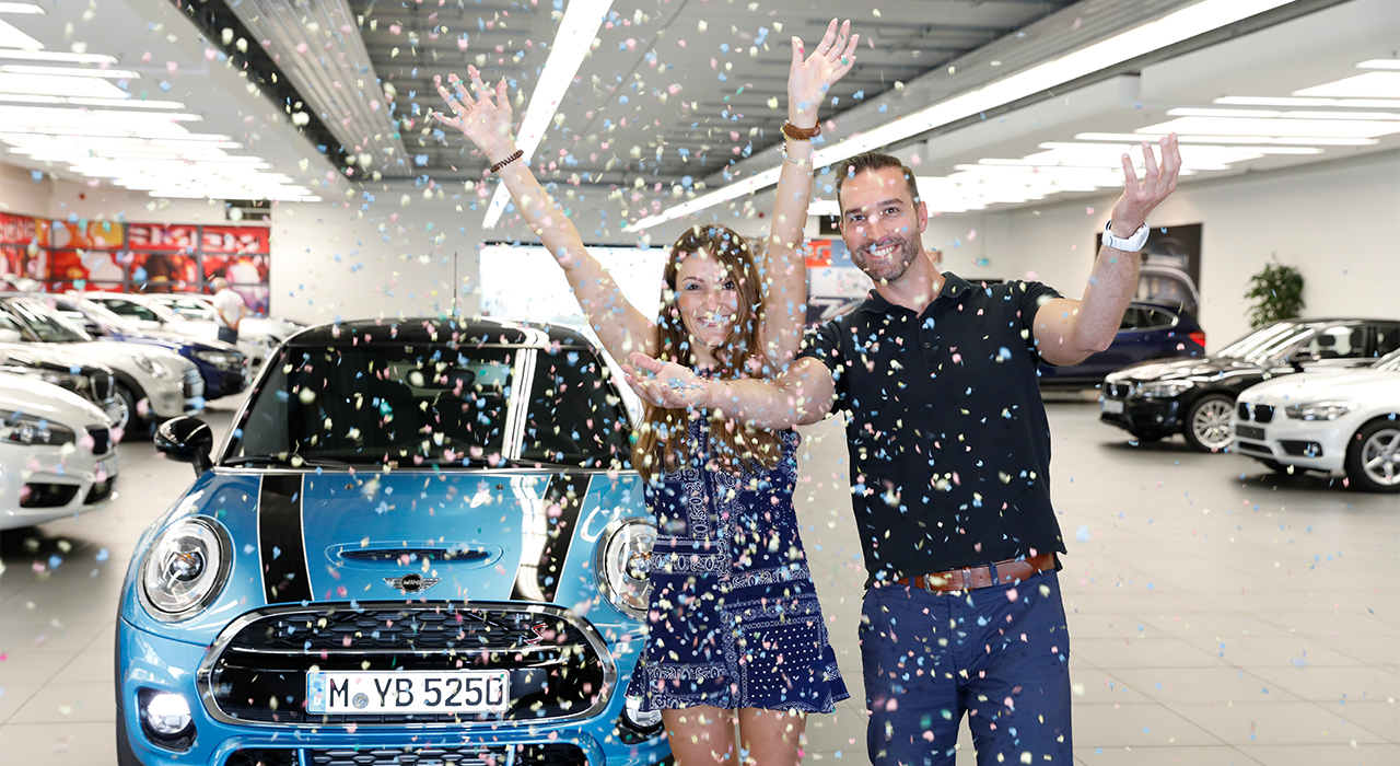 The picture shows two colleagues throwing confetti in the air next to a MINI.