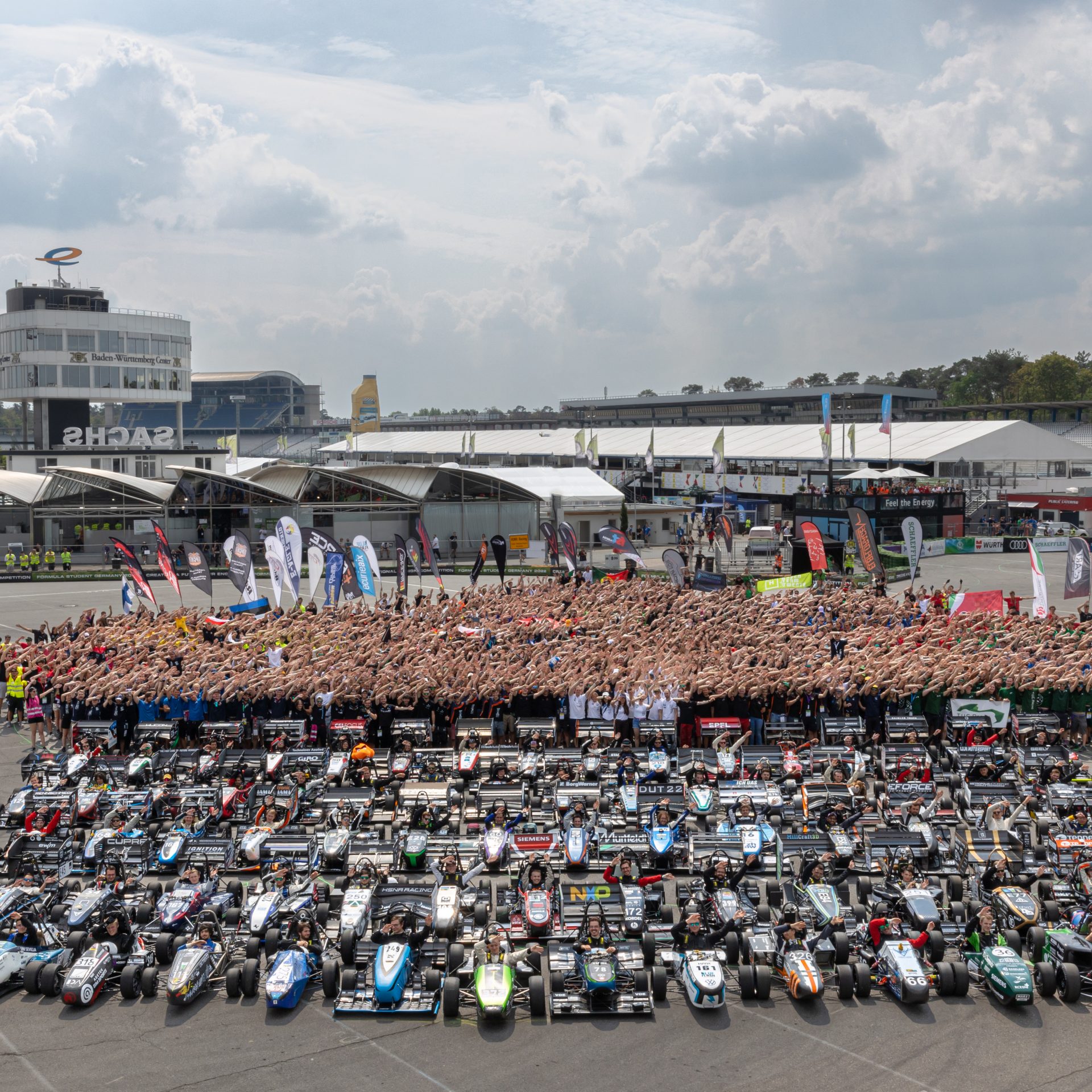 All Formula Student members and their cars are standing together on a huge space, posing for the camera.