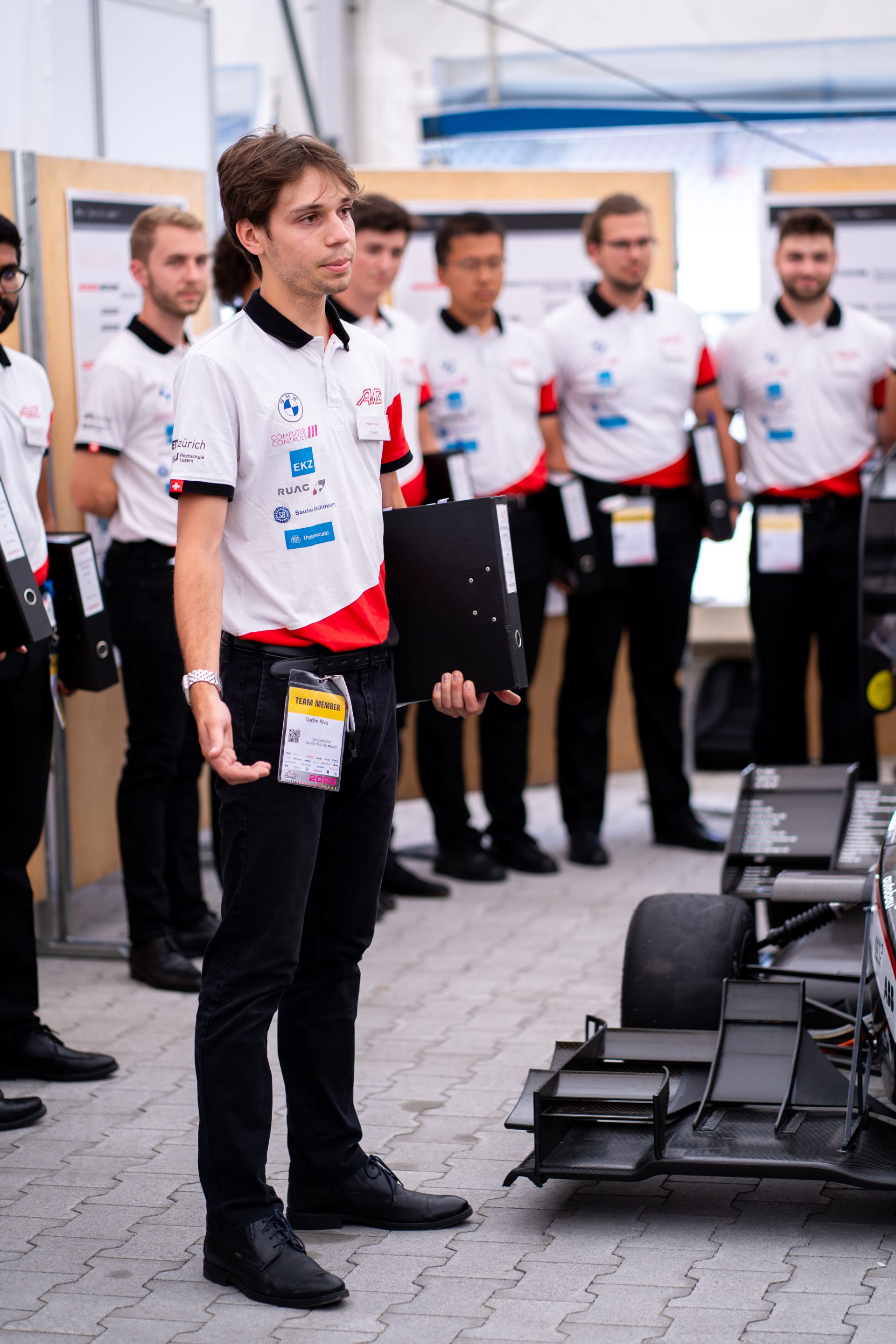 A young man standing next to a racecar with the rest of his team behind him.