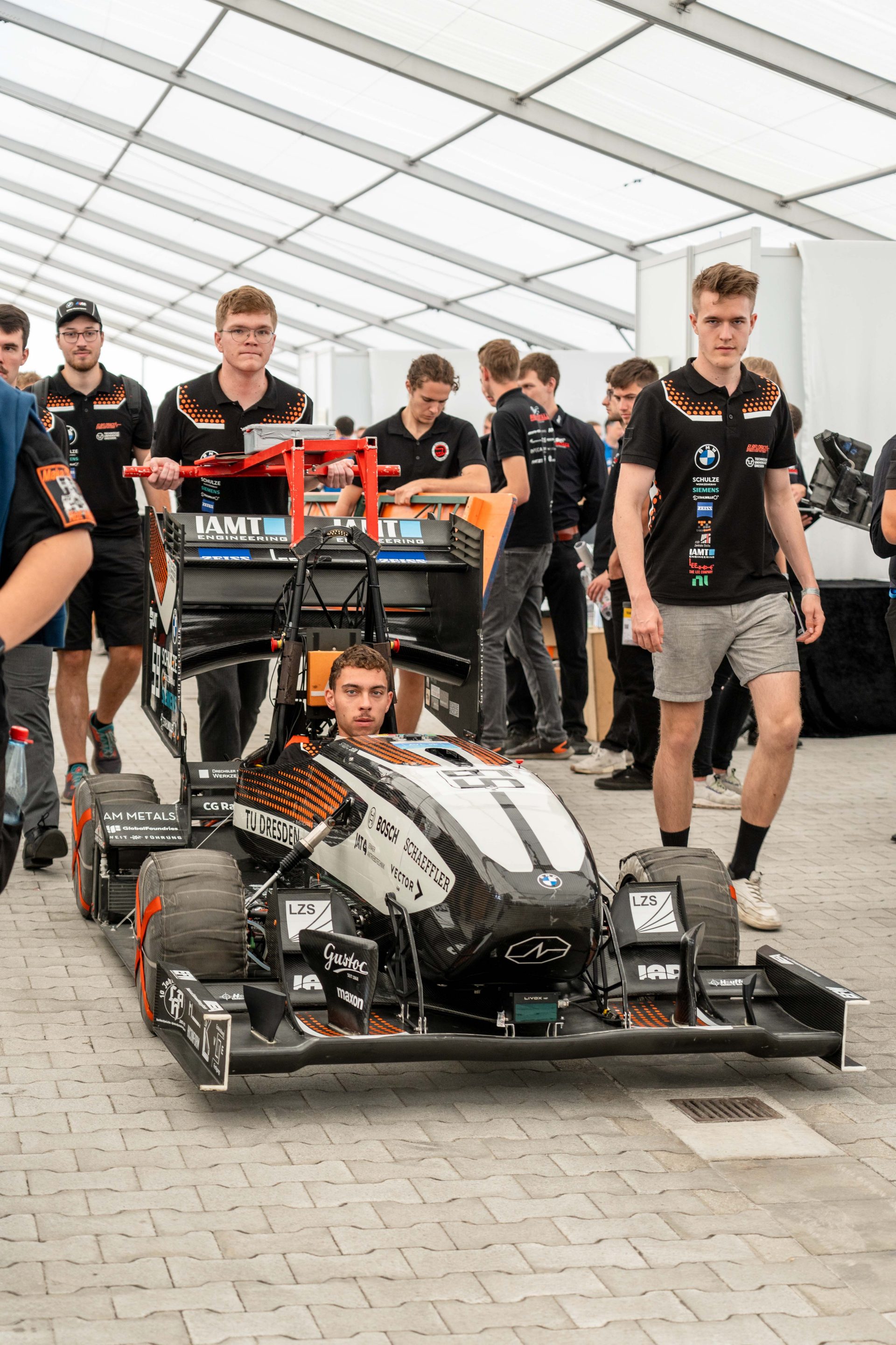 Young man in a racecar with his team standing around him.
