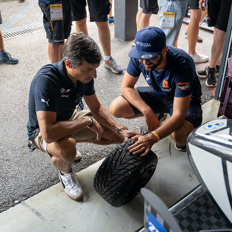 BMW Group Plant Driver Bruno Spengler is inspecting a wheel together with a student.