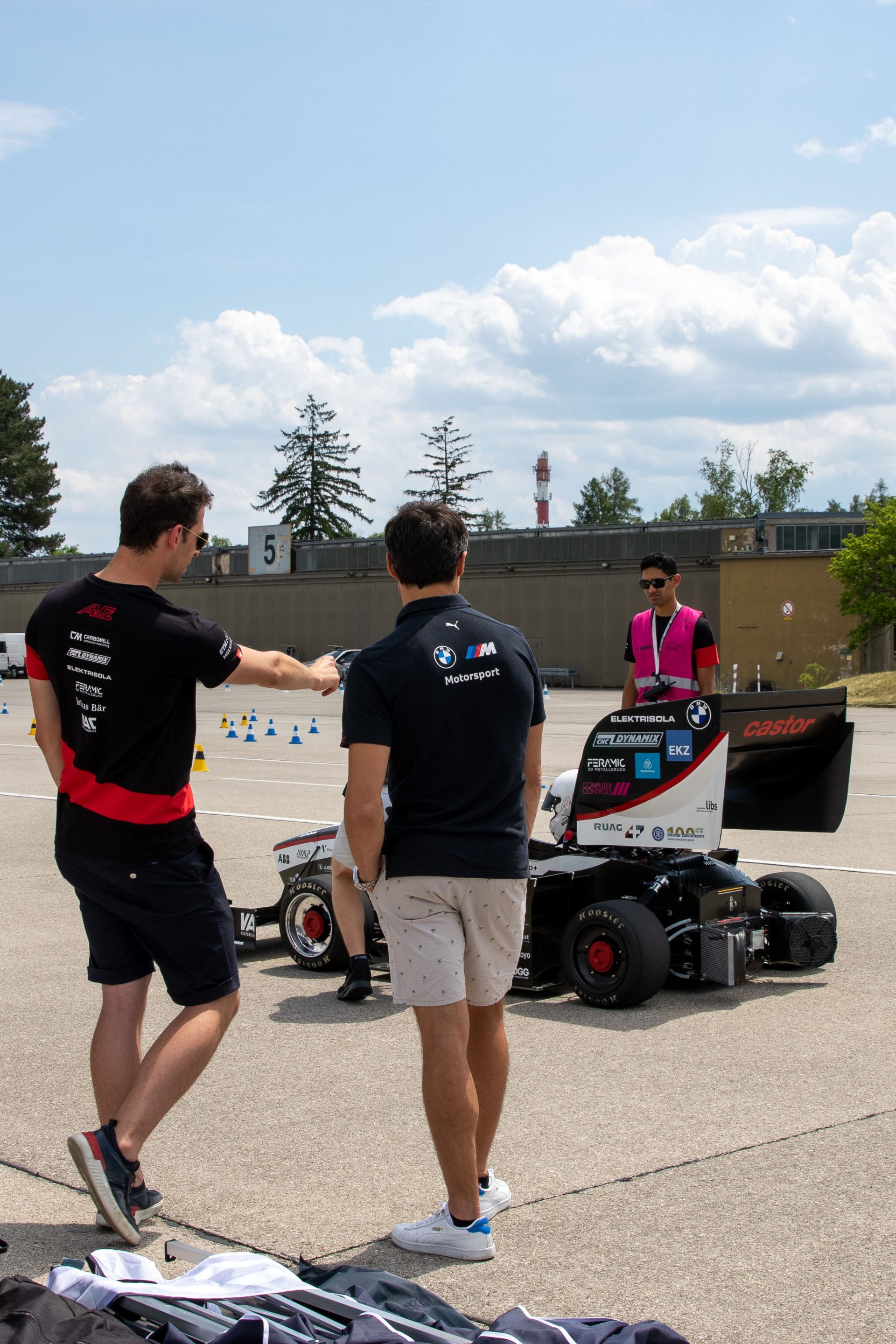 Three man standing on the test track with their racecar.