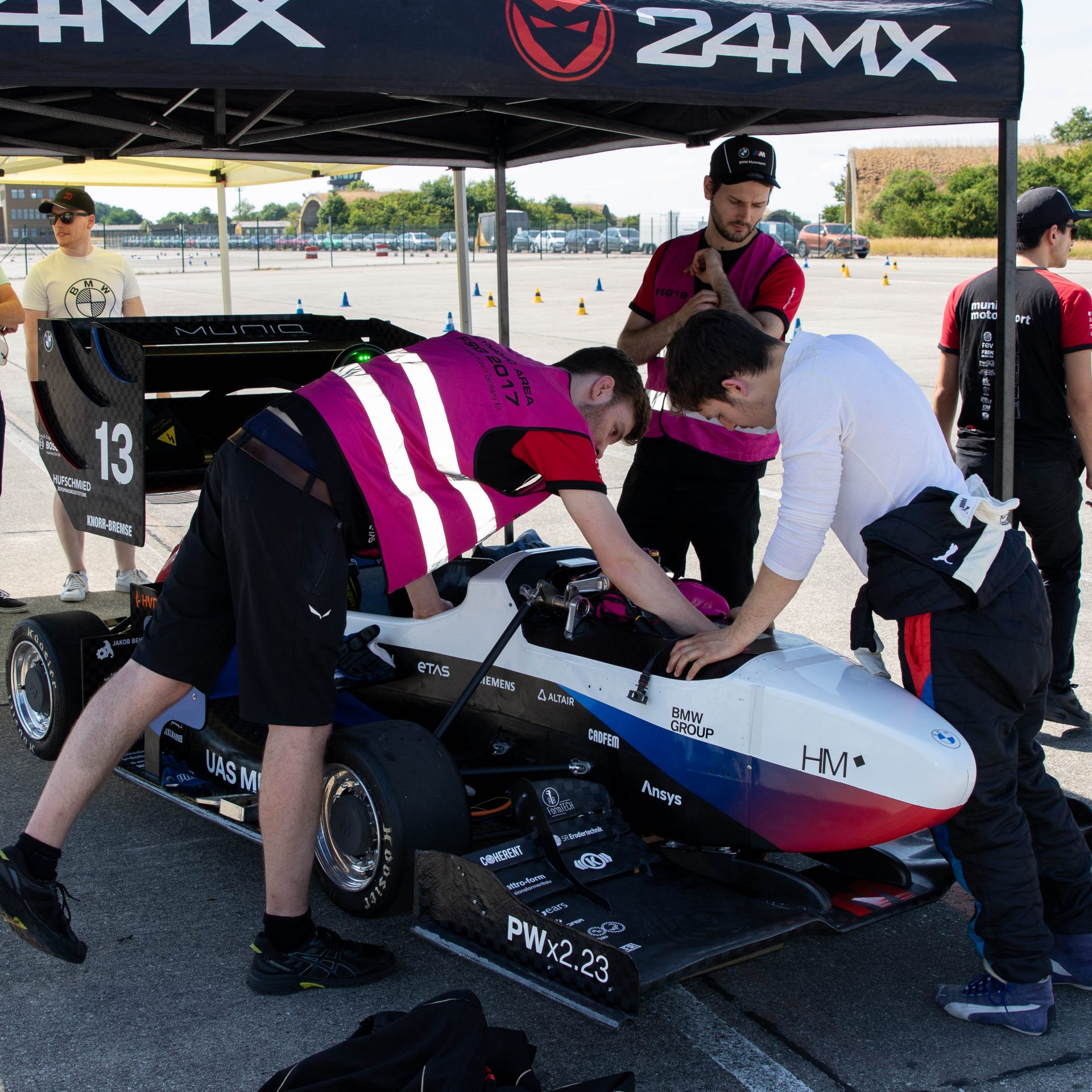 Three young men standing around a racecar, inspecting it.