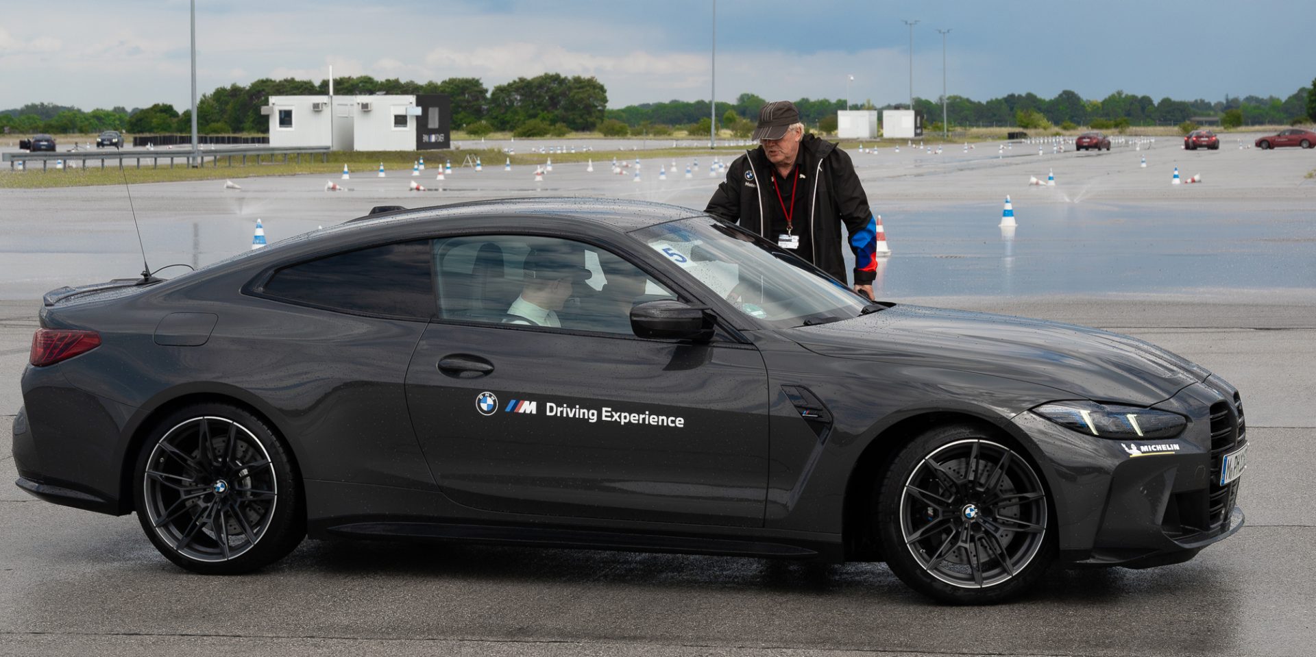 An old man standing behind a BMW car.