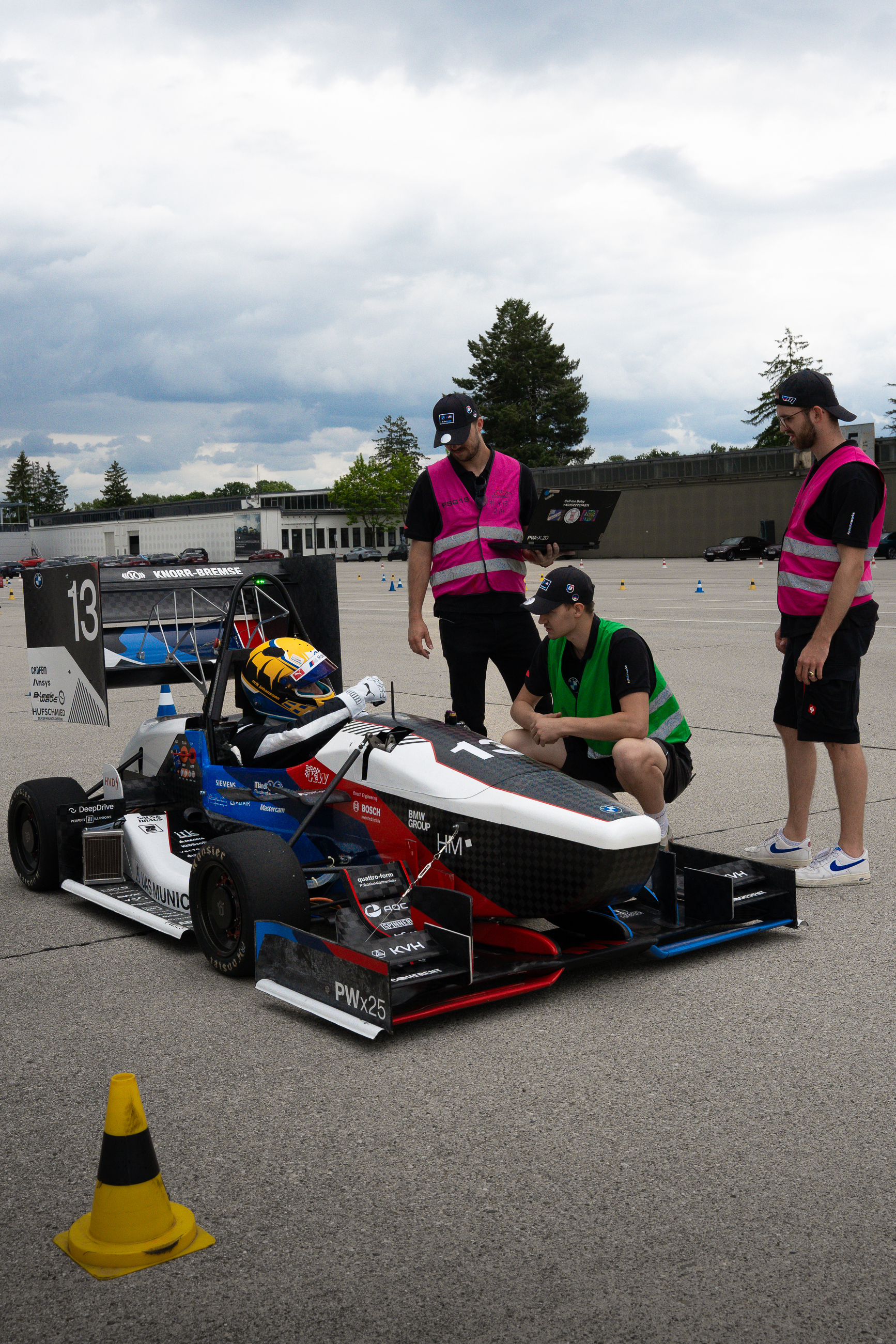 A driver in a race car talking to three people with a warning vest.
