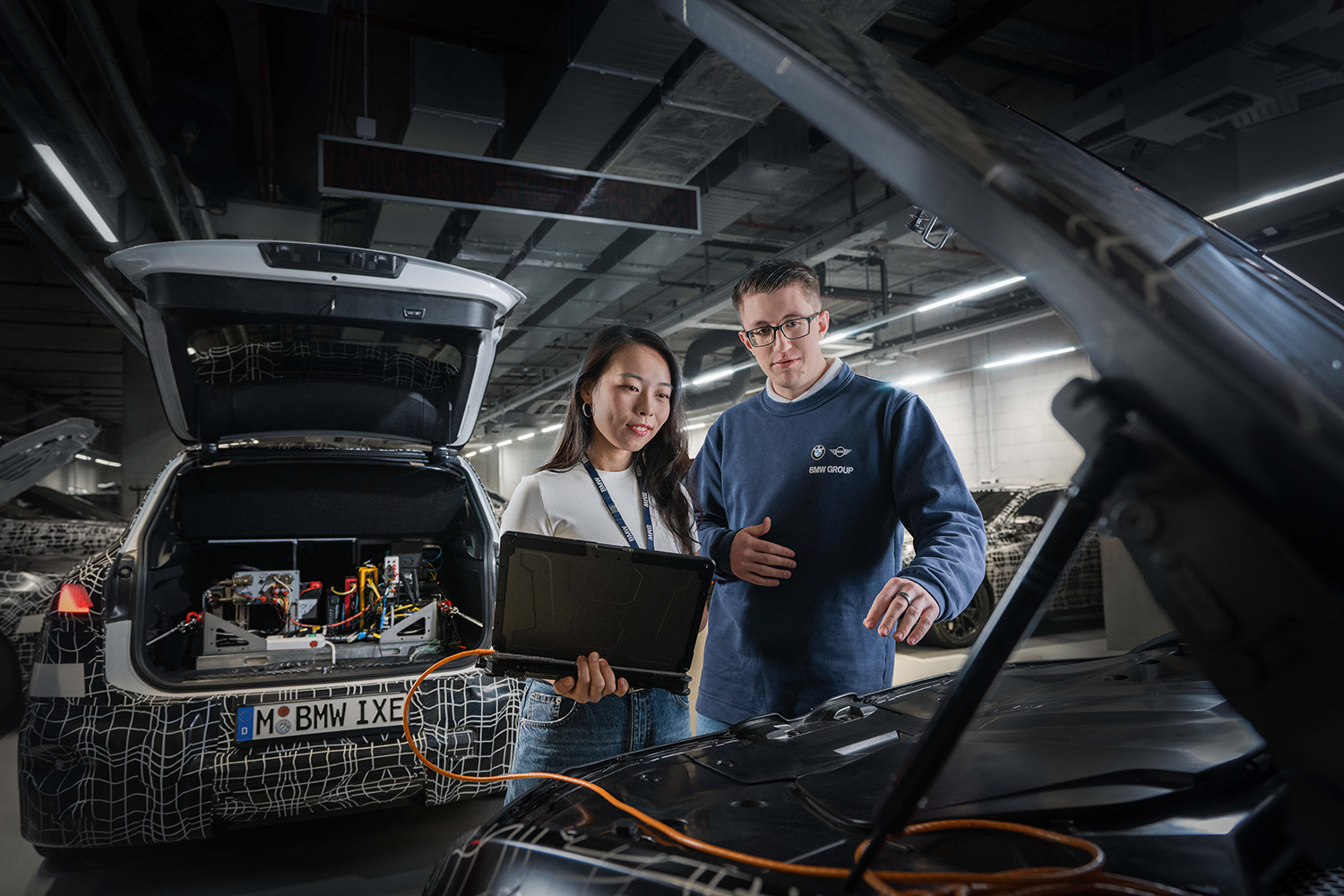 Two IT colleagues, a woman and a man, are working on a laptop at a track in the boot of a prototype vehicle.
