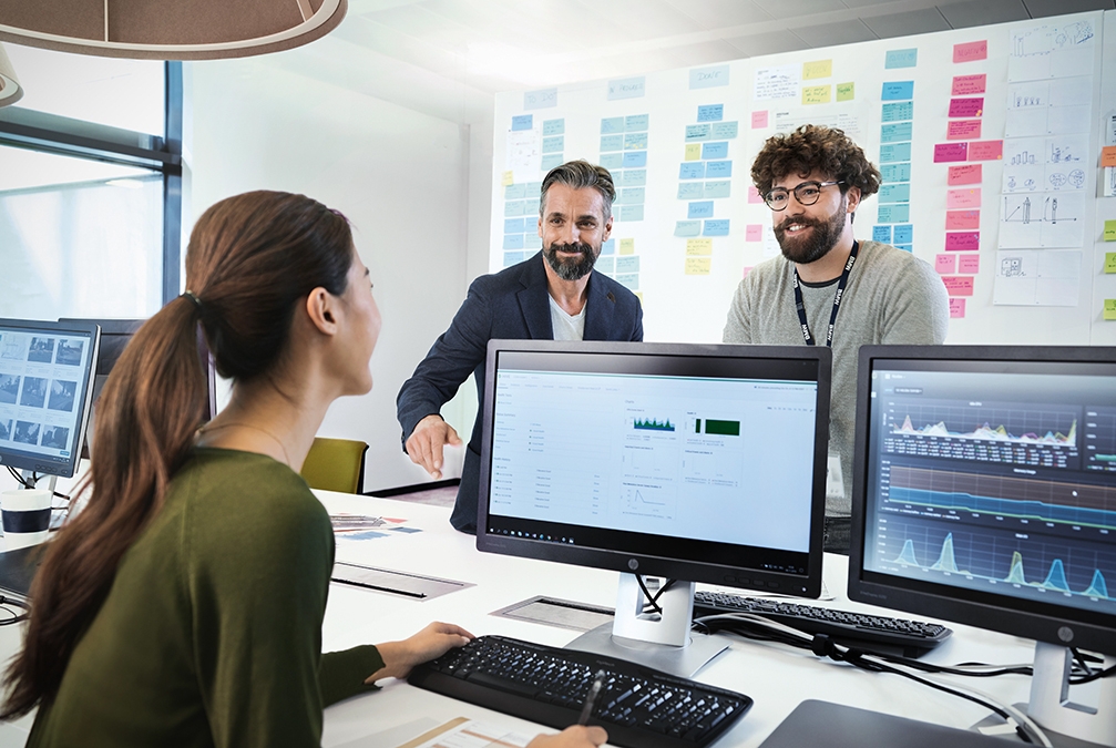 Three colleagues at the BMW Group are having a collaborative conversation in a modern office setting.