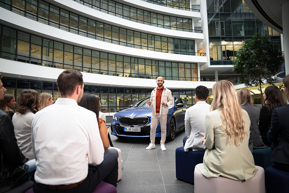 A person gives a talk to an audience in front of a BMW M5.