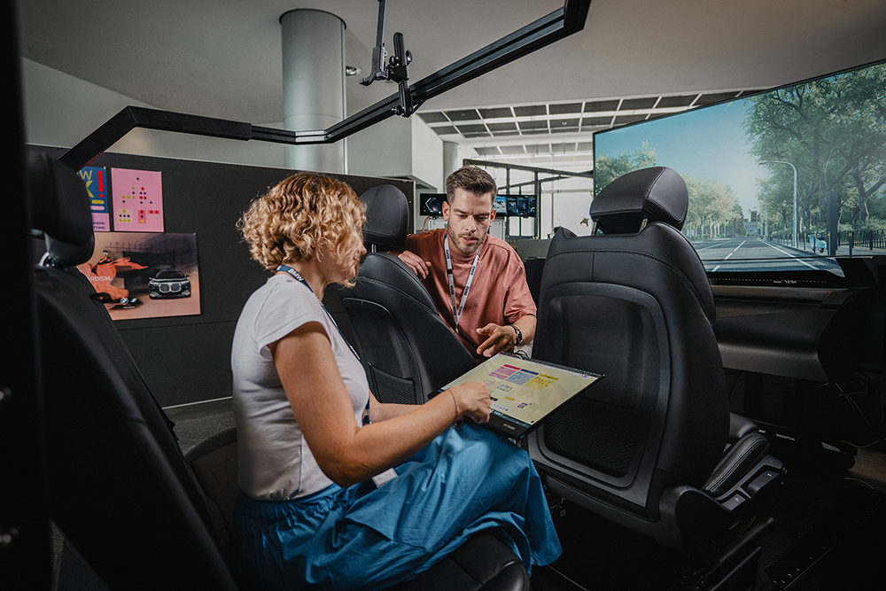 Two employees sit in a driving simulator.