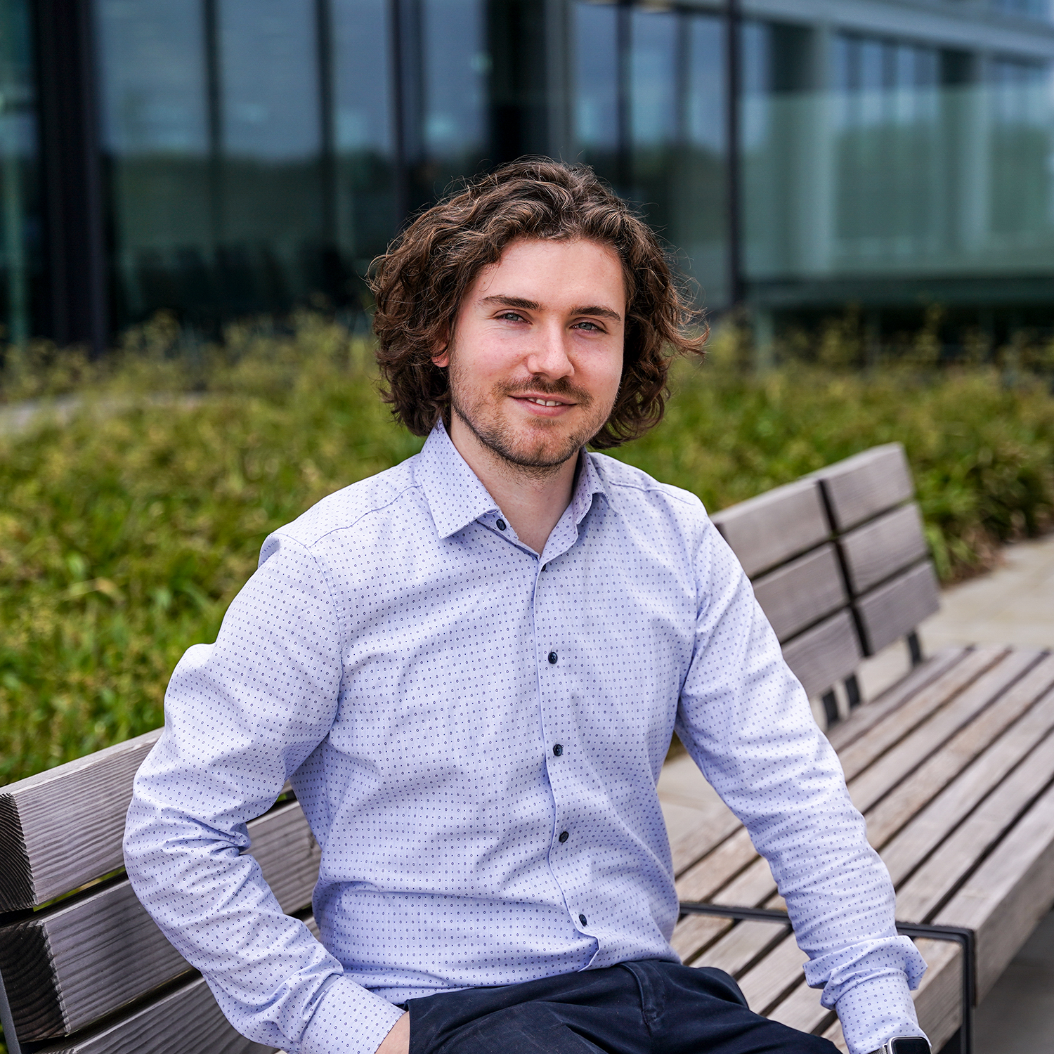 A young man sitting outside smiling at the camera.