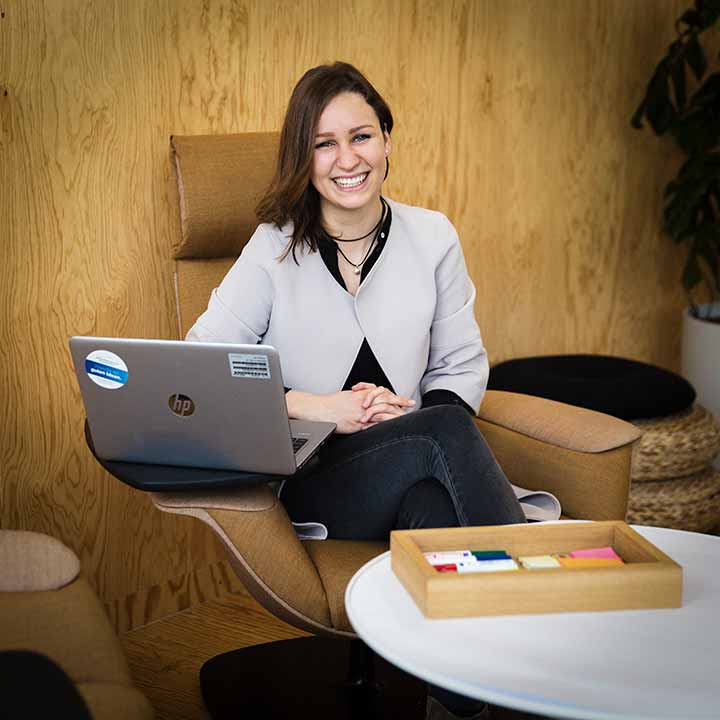A woman seating in front a laptop and smiling at the camera. 